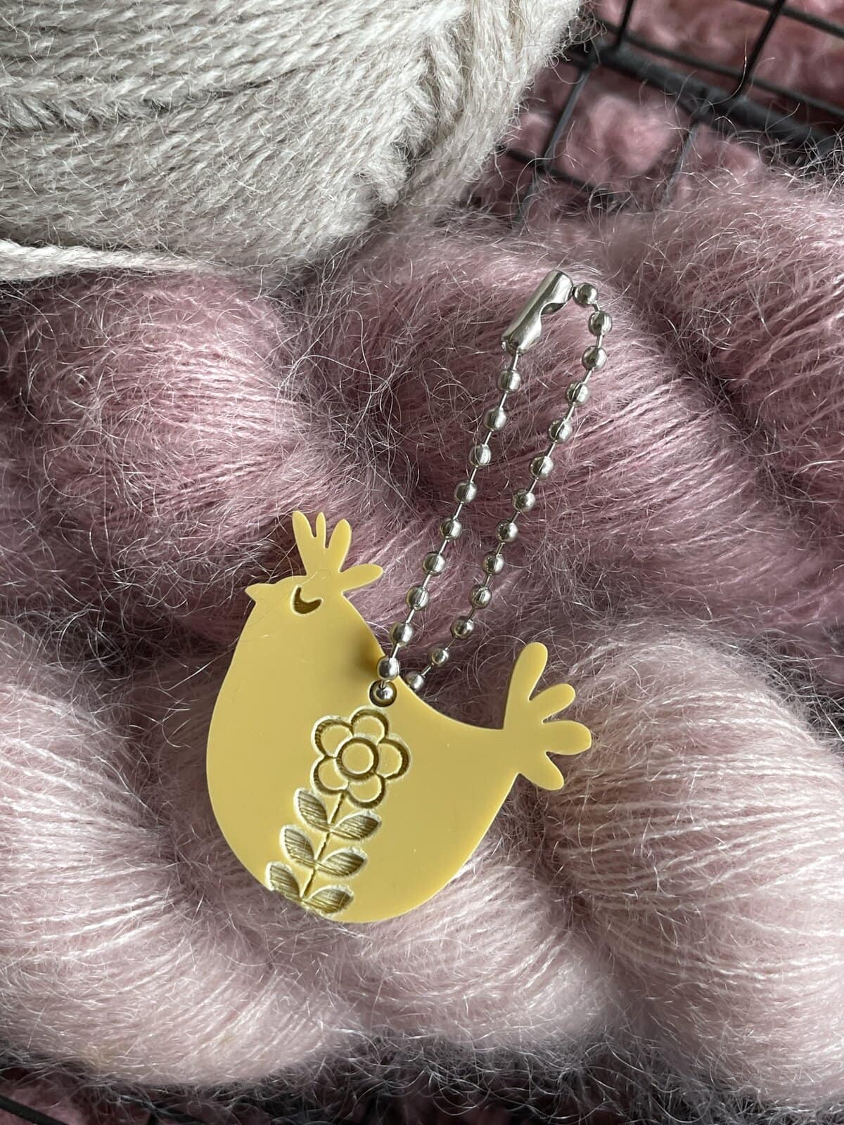 Bright yellow chicken-shaped yarn accessory with a flower design, on a cozy ball of pink and cream yarn.