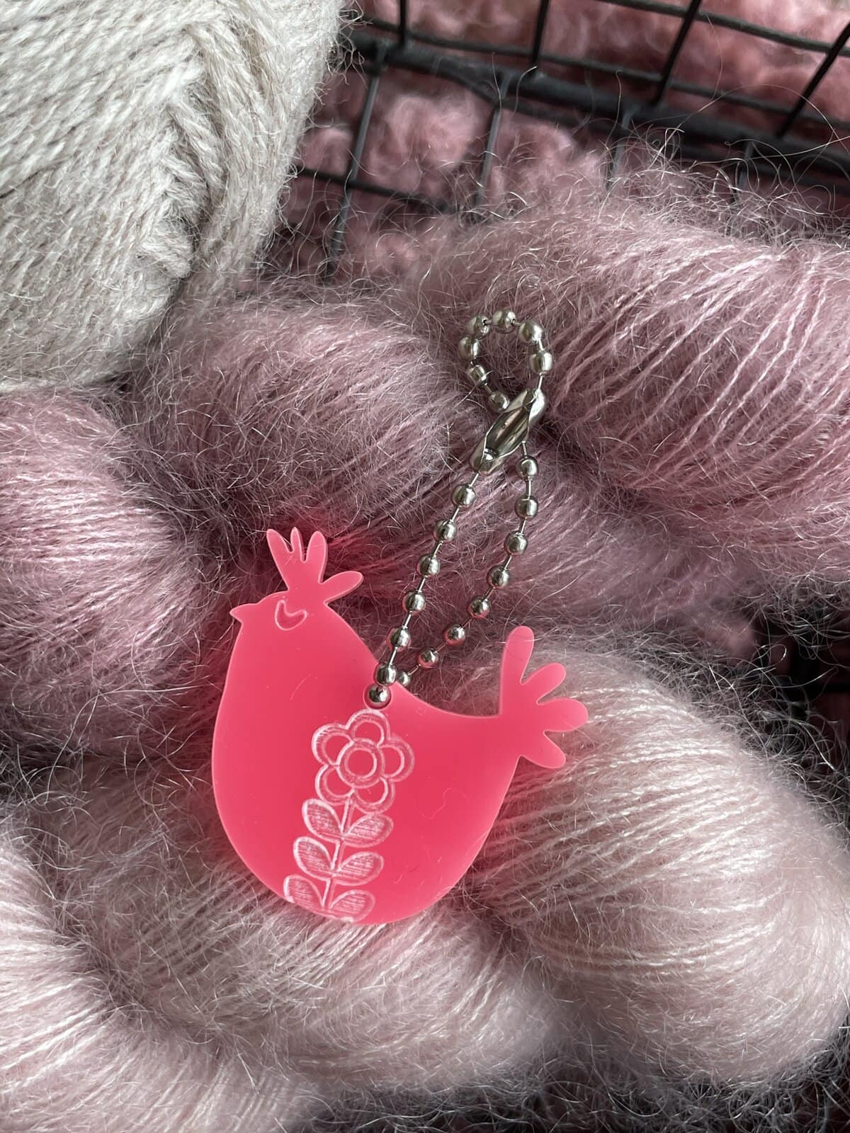 Bright pink plush chicken keychain with floral design, perfect for yarn and craft enthusiasts.