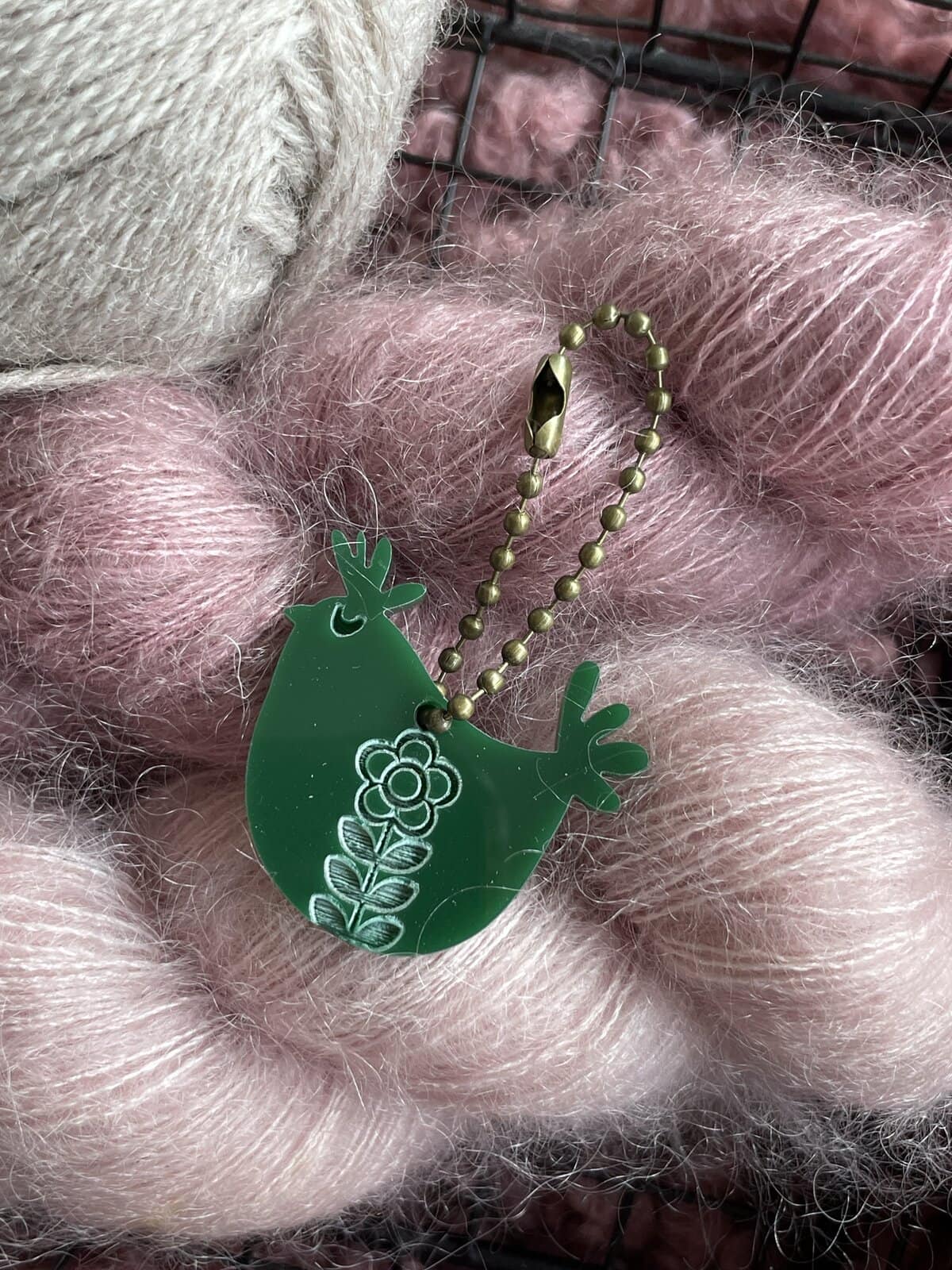 Bright green cactus keychain with floral design on soft pink and cream yarn balls.