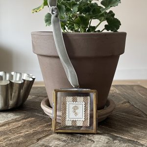 Soft silver satin ribbon with cross-stitch embroidery charm on rustic wooden table.