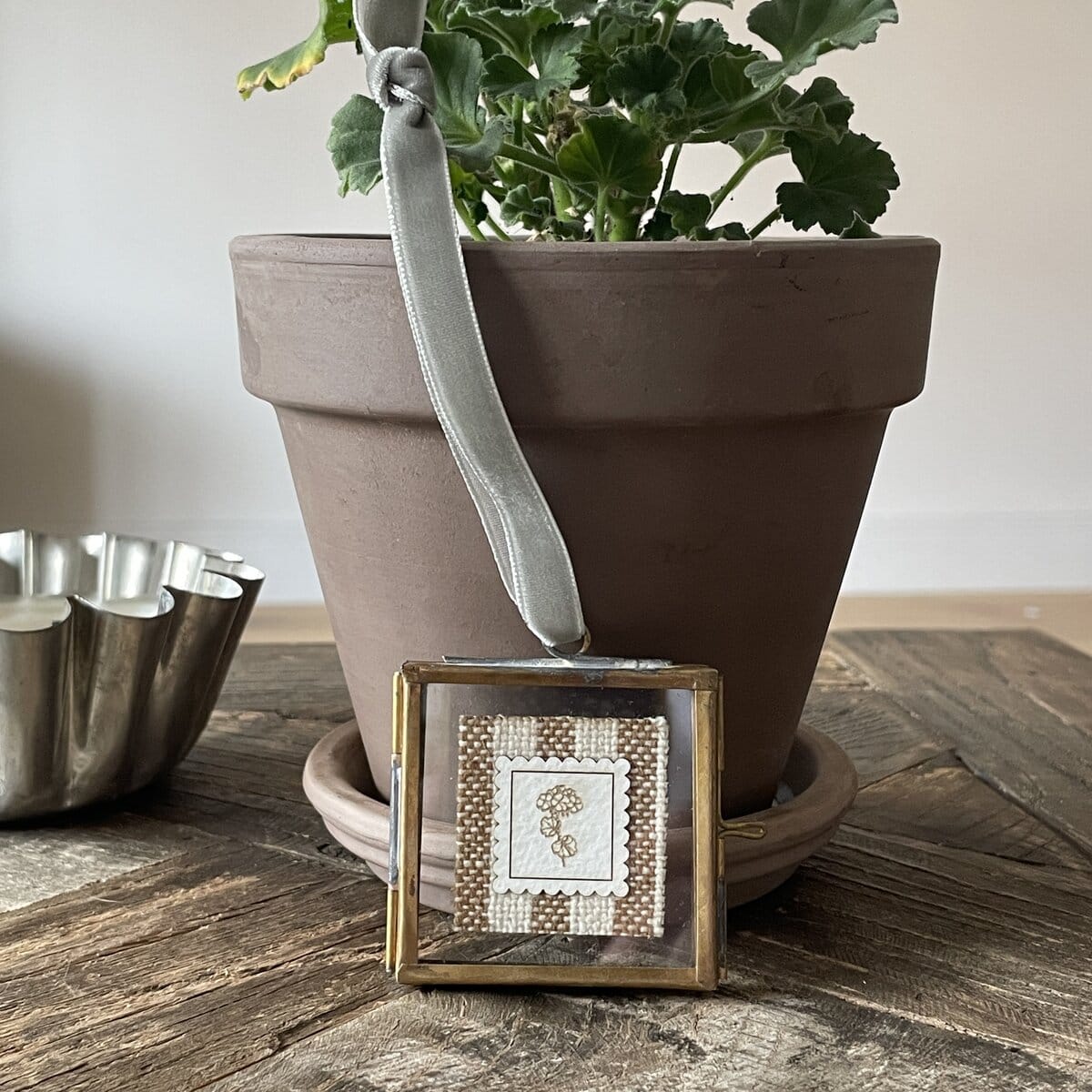 Soft silver satin ribbon with cross-stitch embroidery charm on rustic wooden table.