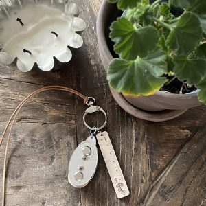 Bright green geranium plant with white flower, wood table candle, and keychain with measuring ruler - cozy craft space.