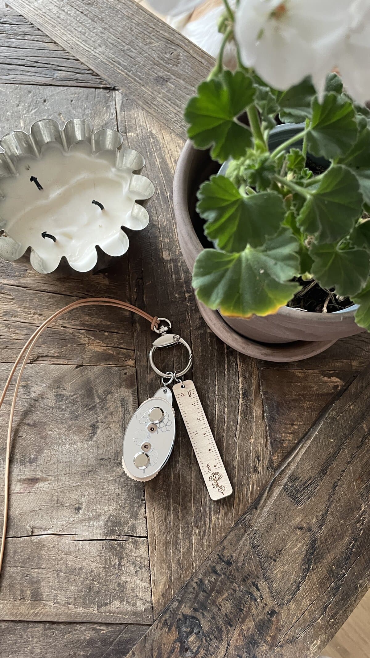 Bright green geranium plant with white flower, wood table candle, and keychain with measuring ruler - cozy craft space.