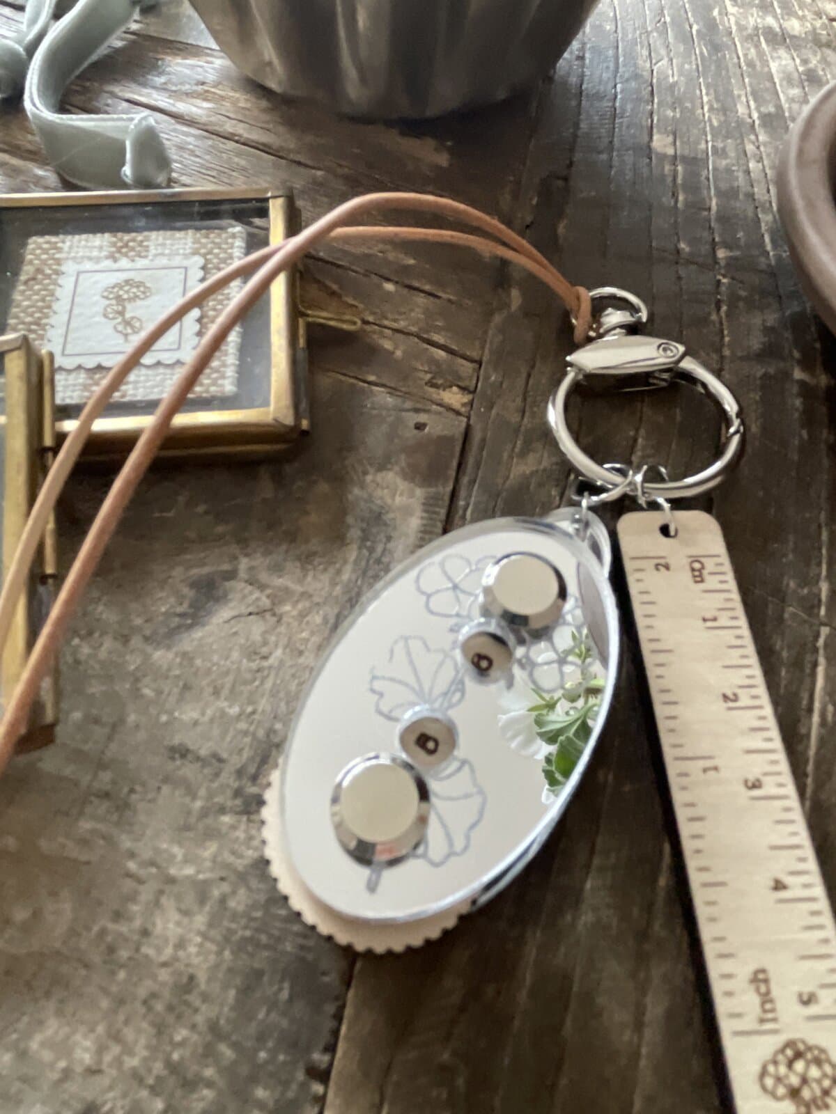 1. Silver keychain with floral design and ruler attached on rustic wooden table.