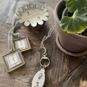 Vintage candle holder and jewelry on rustic wooden table with potted plant, cozy decor elements.