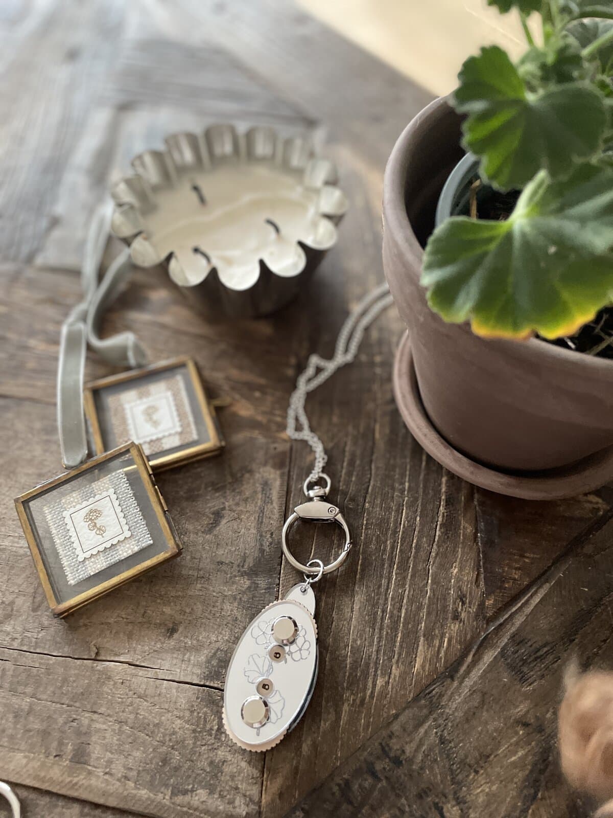Vintage candle holder and jewelry on rustic wooden table with potted plant, cozy decor elements.