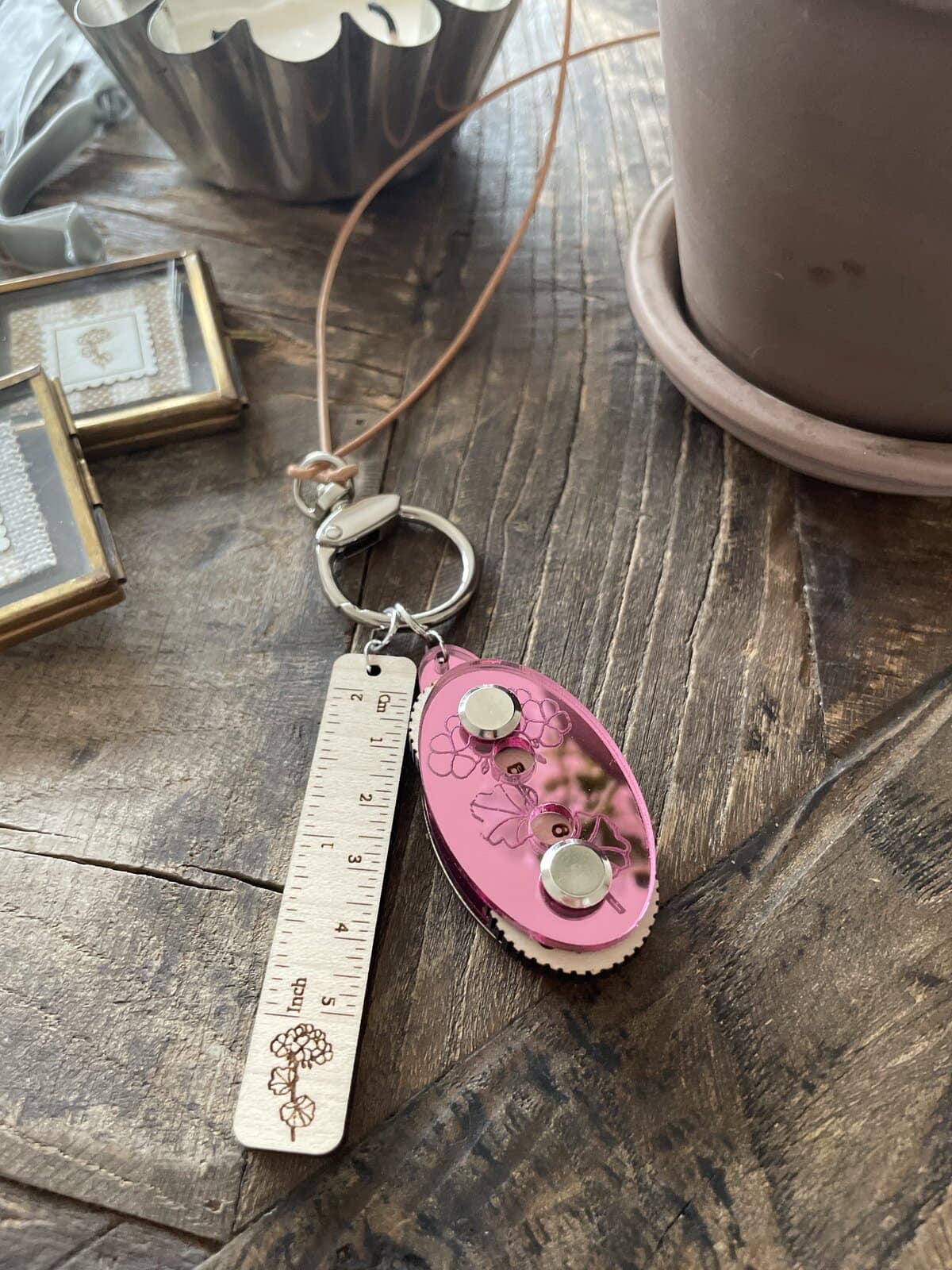 Bright pink floral-themed keychain with ruler and mirror accessories for knitting or crafting.