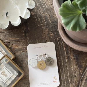 Silver and gold engraved charm keychain with floral design, displayed on a white card from Unwrapped Yarn.