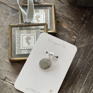 Silver jewelry gift set with engraved flower pendant and earrings, presented on a white card on rustic wood surface.