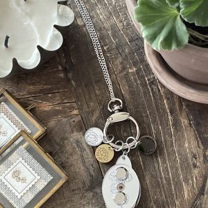 Shiny silver keychain with multiple charms on a rustic wooden surface, surrounded by candles and potted plants.