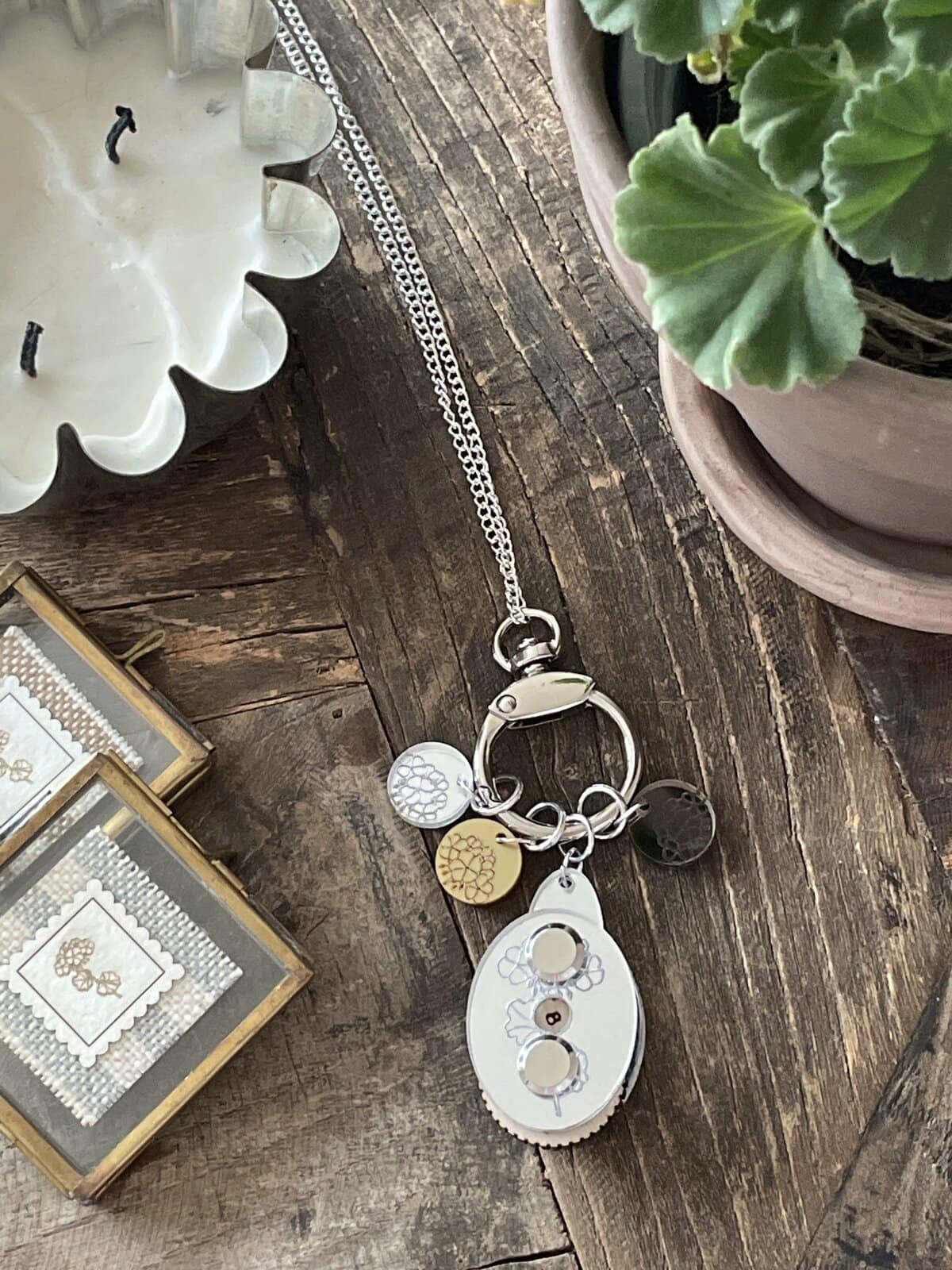 Shiny silver keychain with multiple charms on a rustic wooden surface, surrounded by candles and potted plants.