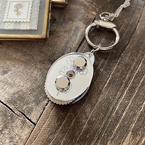 Soft white yarn-inspired keychain with floral design, on rustic wooden background. Perfect for knitting and crochet enthusiasts.
