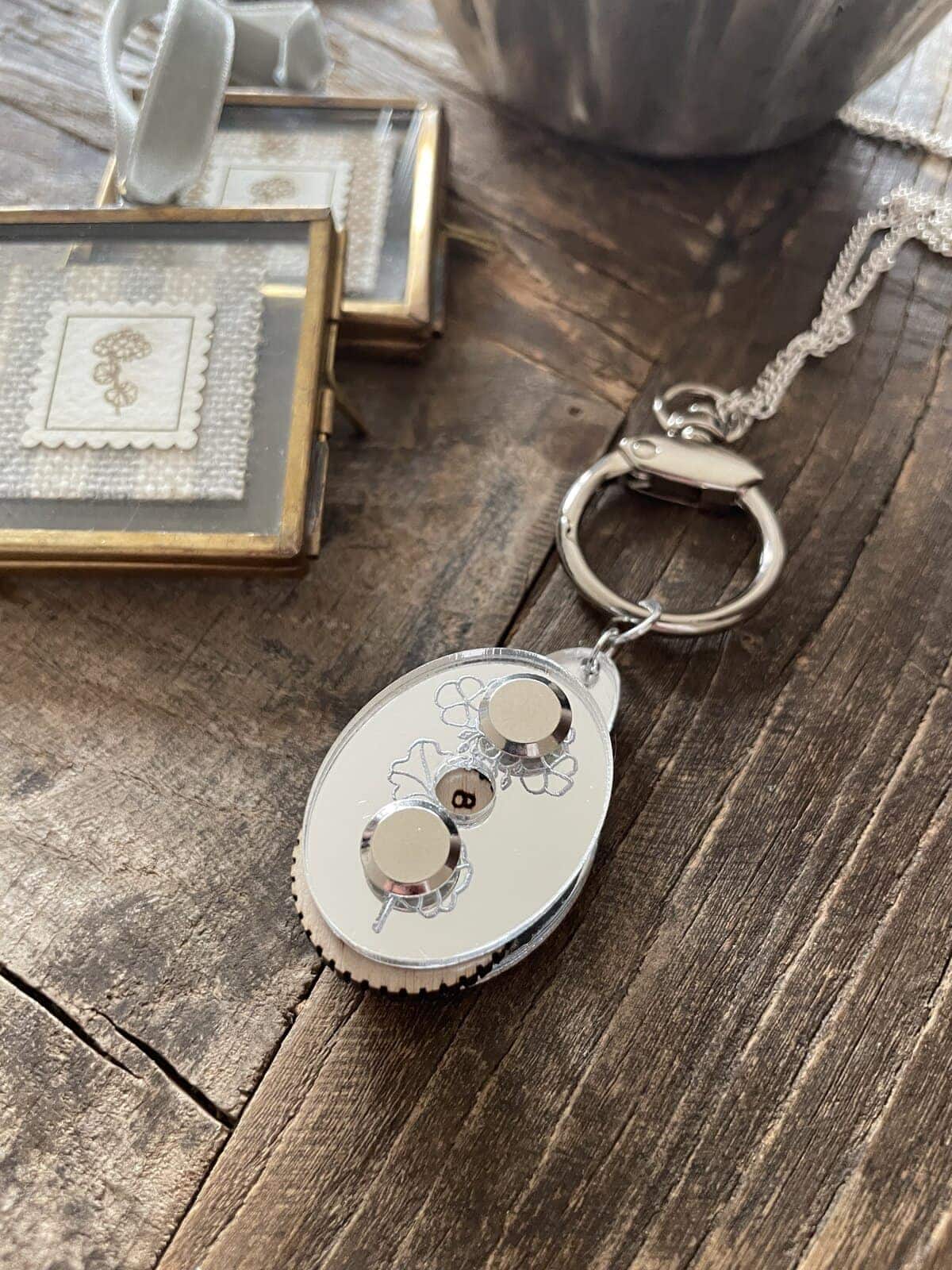 Soft white yarn-inspired keychain with floral design, on rustic wooden background. Perfect for knitting and crochet enthusiasts.