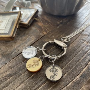Silver keychain with engraved grapevine charms on rustic wooden surface.