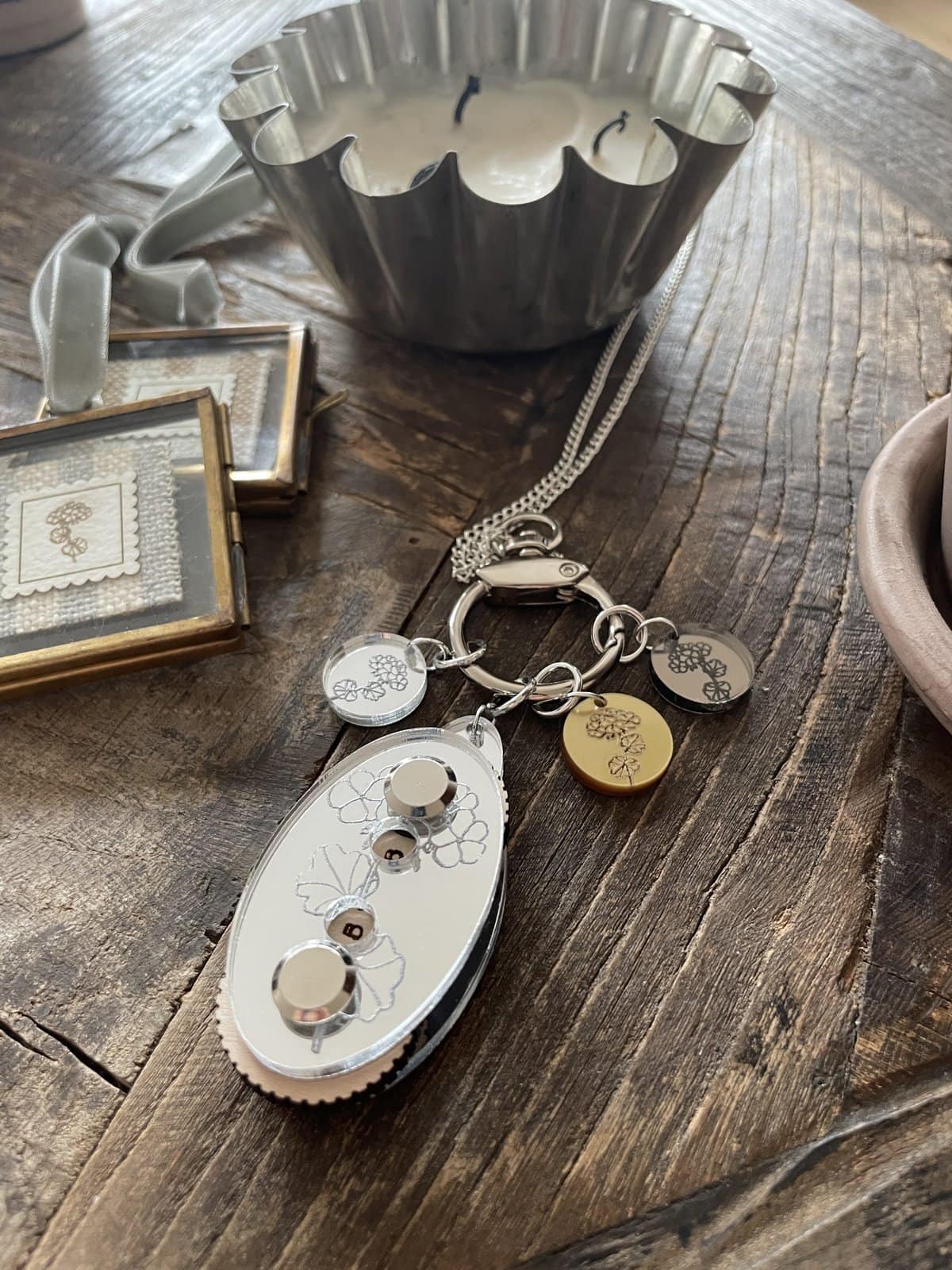 Elegant silver jewelry keychain with floral engraving, displayed on rustic wooden surface.