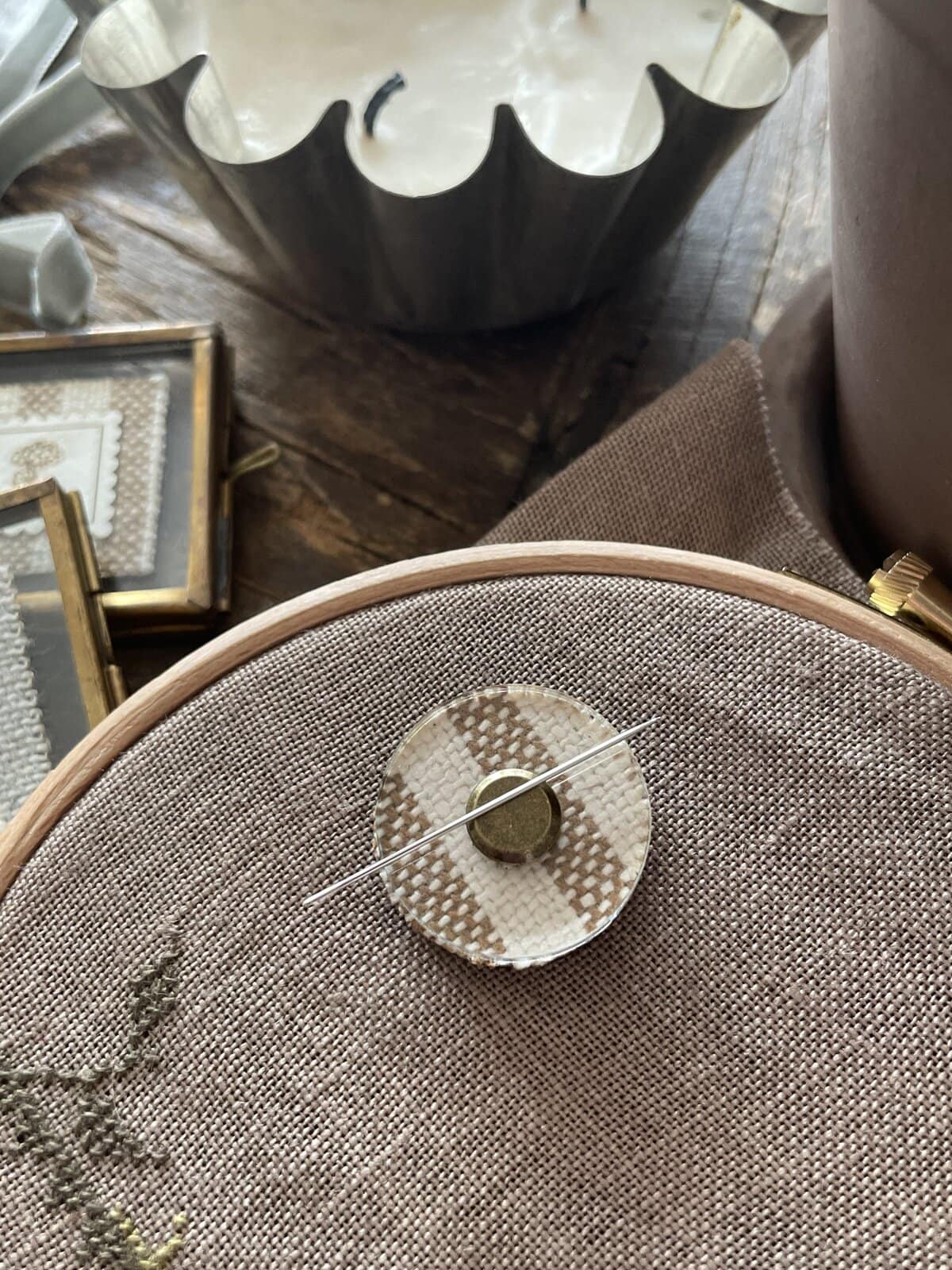 Soft beige embroidery hoop with needle and cream-colored woven fabric, surrounded by vintage decor.