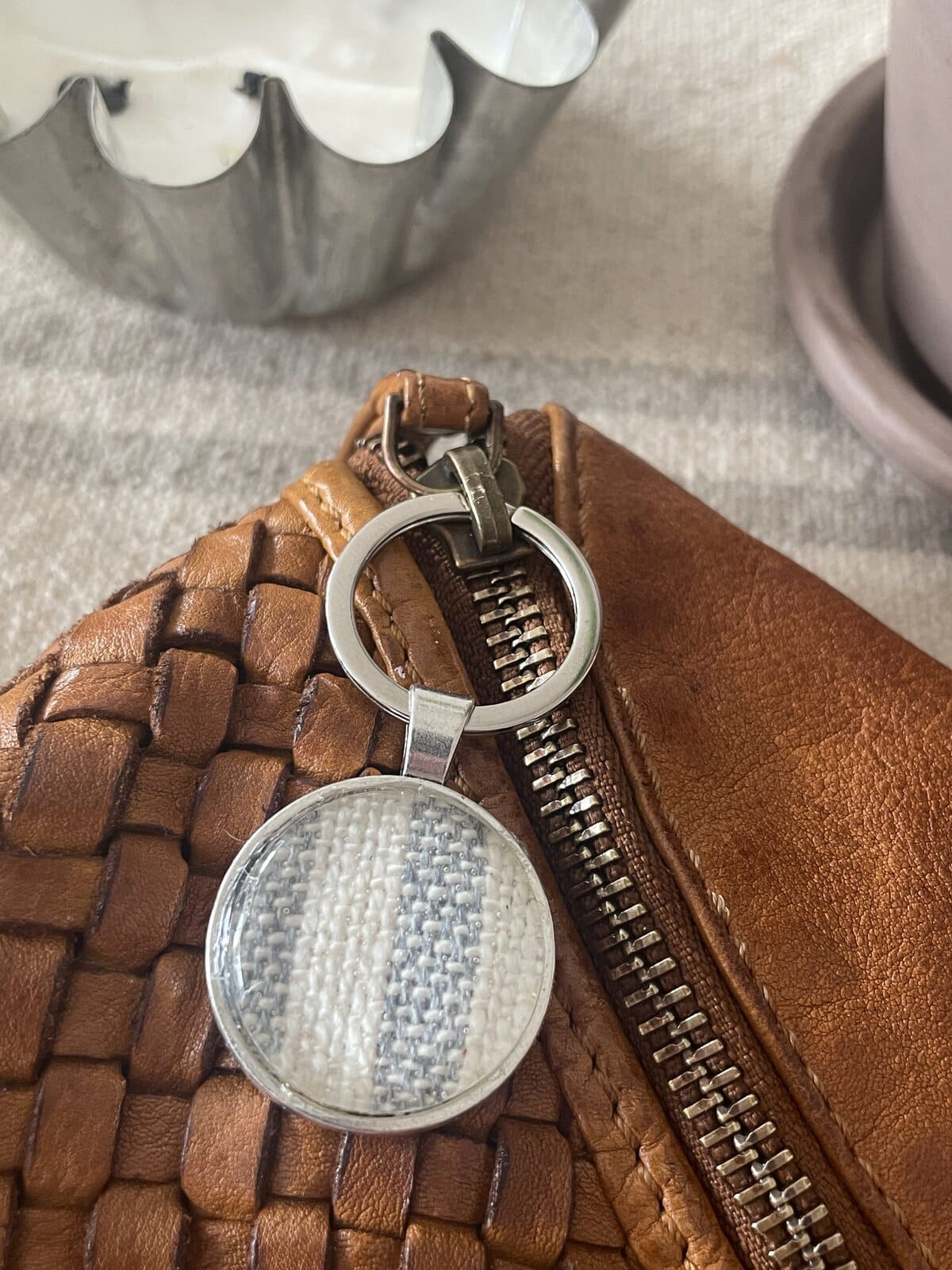 Amulet with woven texture hanging from a leather bag with a zipper, close-up detail.