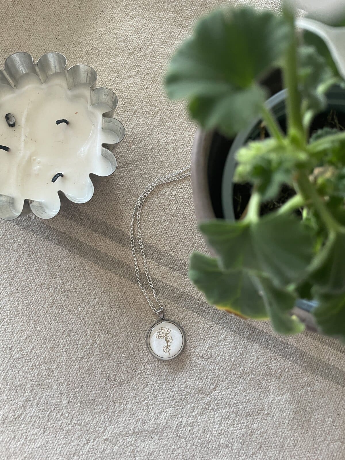 Delicate silver necklace with tree pendant on beige fabric background.
