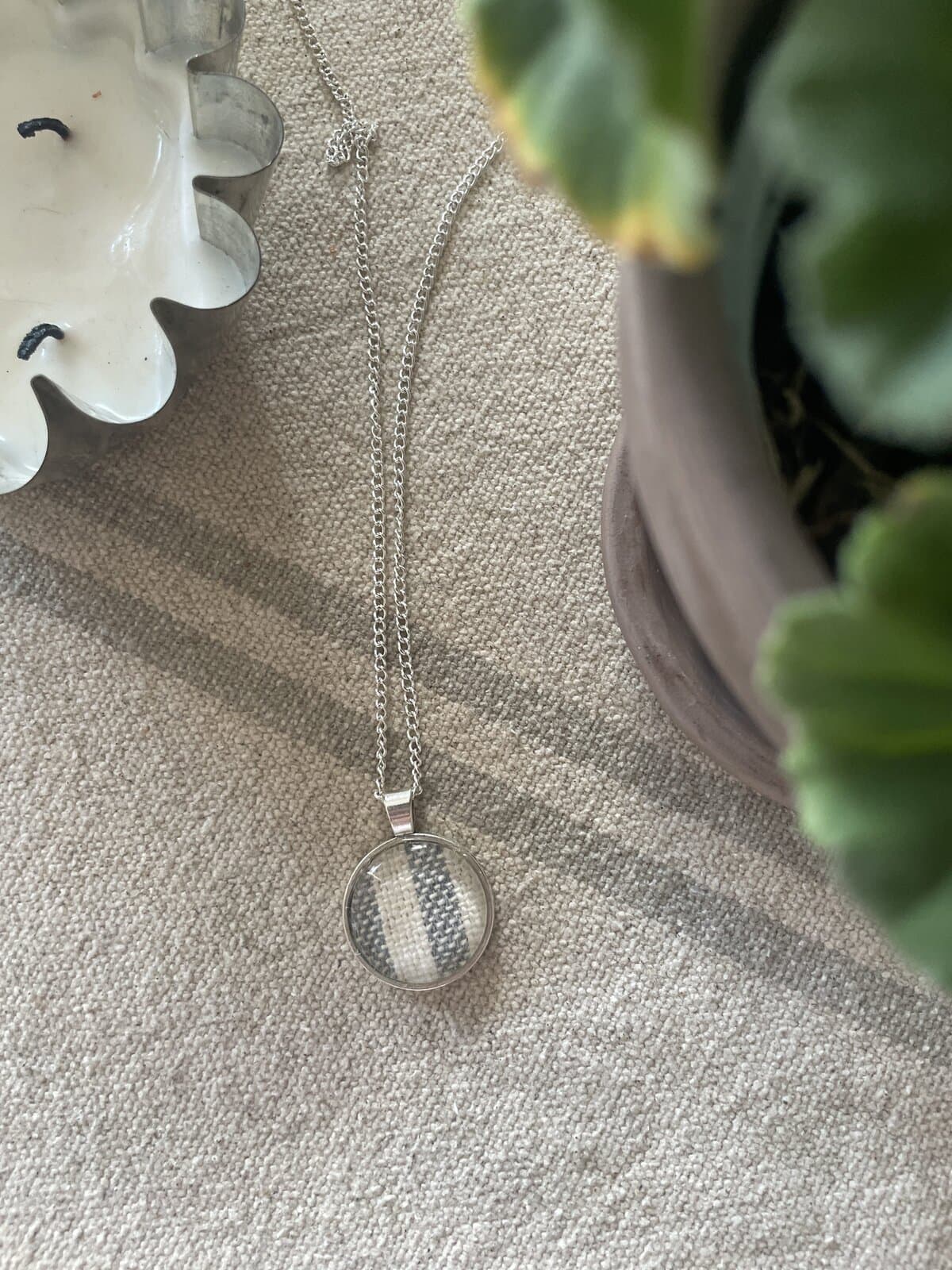 Delicate silver necklace with circular pendant, displayed on textured linen fabric.