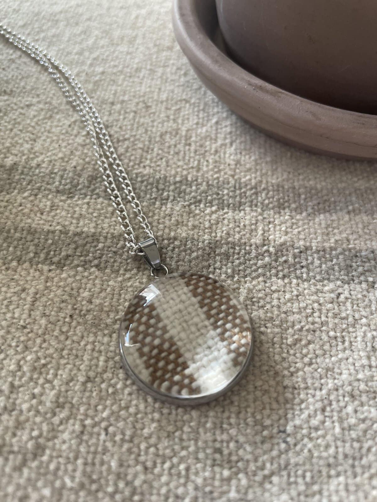 Shimmering round pendant necklace with woven pattern on a silver chain.