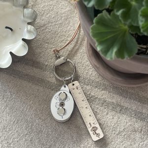 Silk floral keychain with ruler and flower design on a beige textured fabric.