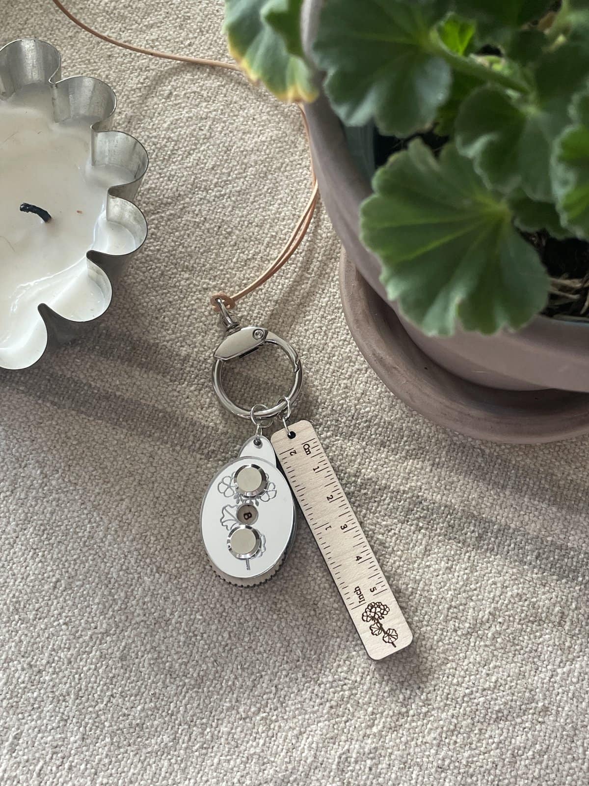 Silk floral keychain with ruler and flower design on a beige textured fabric.