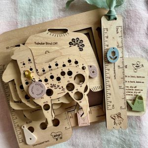 Colorful wooden yarn gauge and tools for knitting and crochet projects on soft pastel cloth.