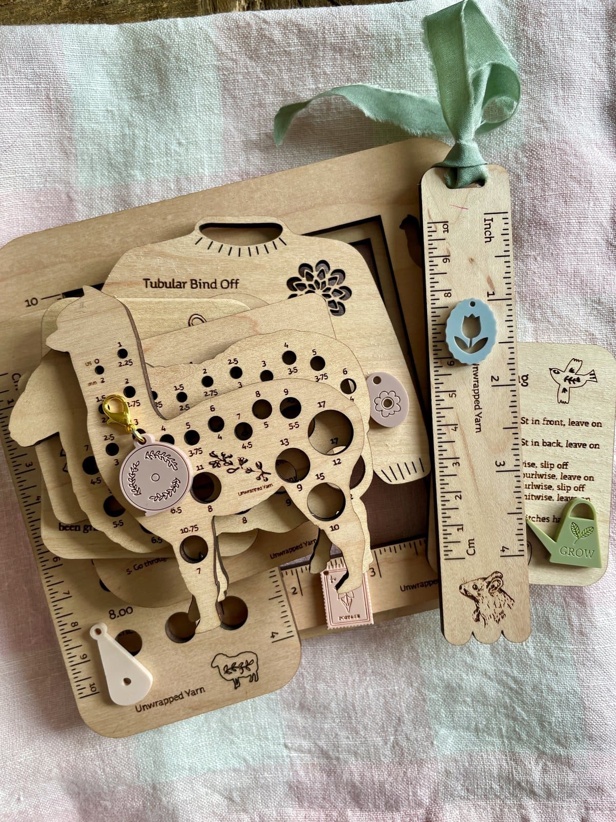 Colorful wooden yarn gauge and tools for knitting and crochet projects on soft pastel cloth.