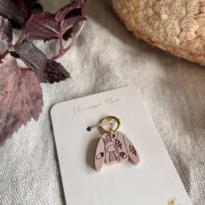 Delicate pink clay keychain with nature-inspired design, tied to Unwrapped Yarn packaging.