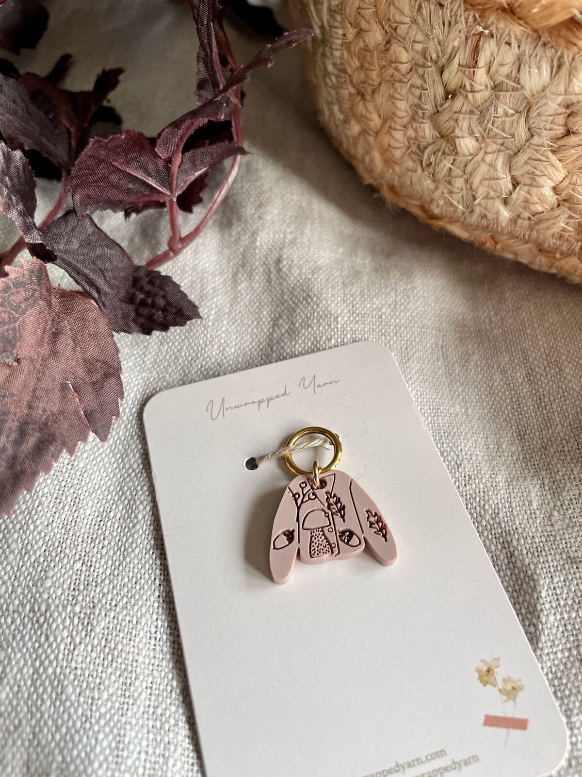 Delicate pink clay keychain with nature-inspired design, tied to Unwrapped Yarn packaging.