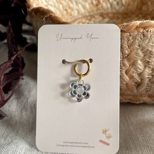 Delicate flower-shaped charm pendant with gold hoop on beige yarn basket for knitting and crochet enthusiasts.