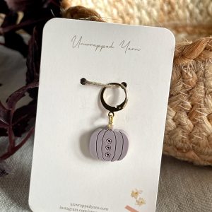 Mini pumpkin-shaped jewelry charm with black line details and small floral accents, on a white card from Unwrapped Yarn.