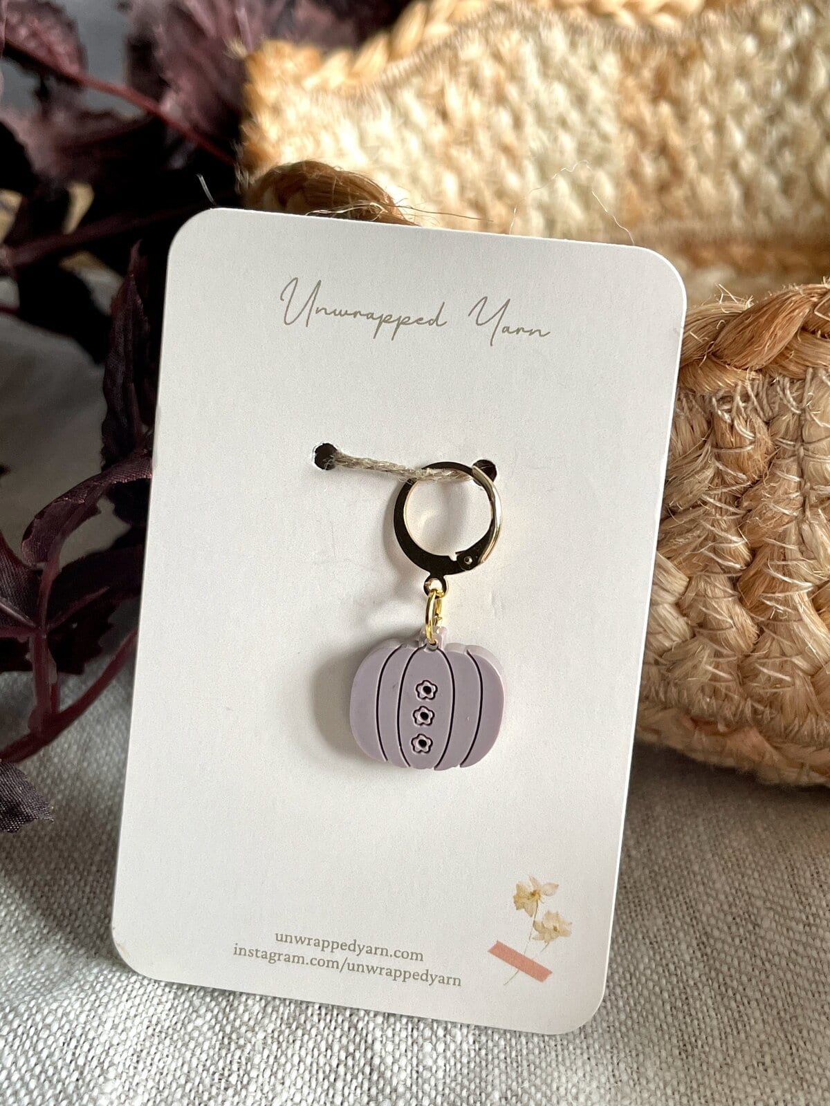 Mini pumpkin-shaped jewelry charm with black line details and small floral accents, on a white card from Unwrapped Yarn.