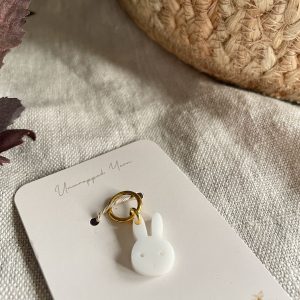 Soft white bunny-shaped zipper charm on a white card, cozy textured fabric background.