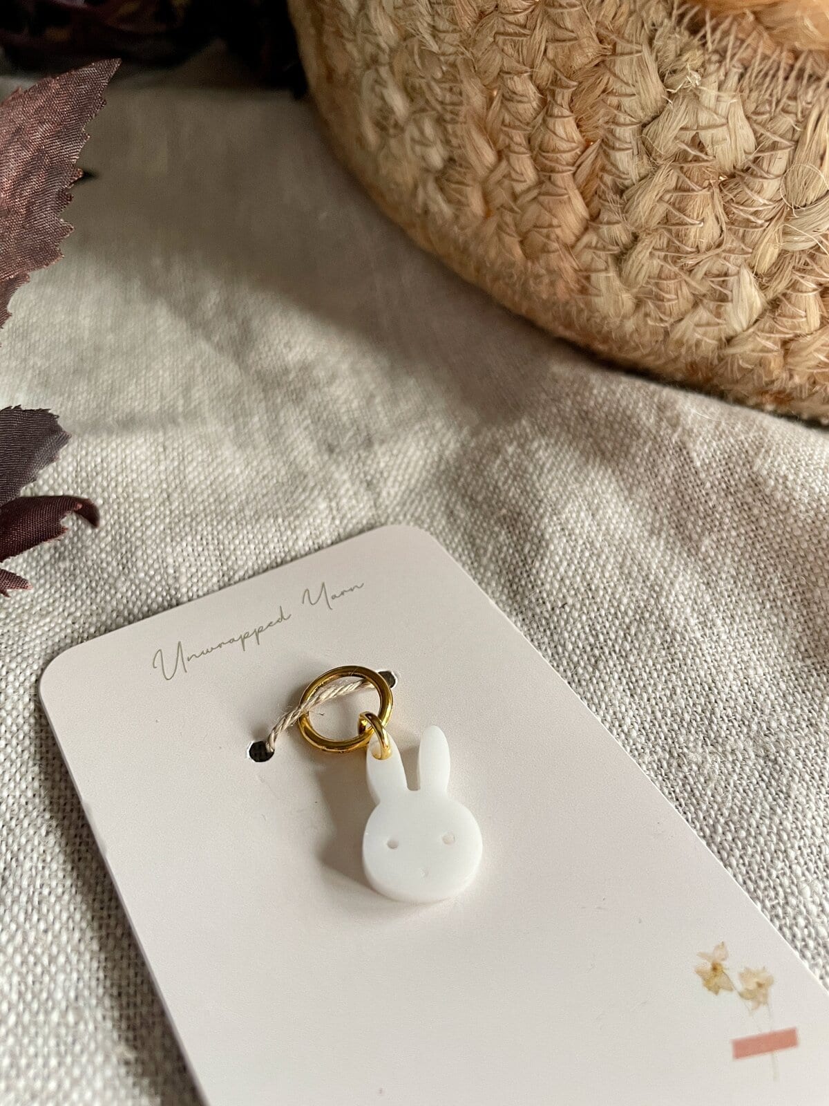 Soft white bunny-shaped zipper charm on a white card, cozy textured fabric background.