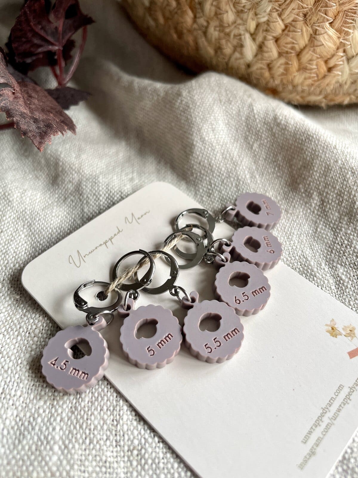 Color-coded stitch marker charms for knitting, labeled 4.5mm and 5.5mm, on a white card with yarn and fabric background.