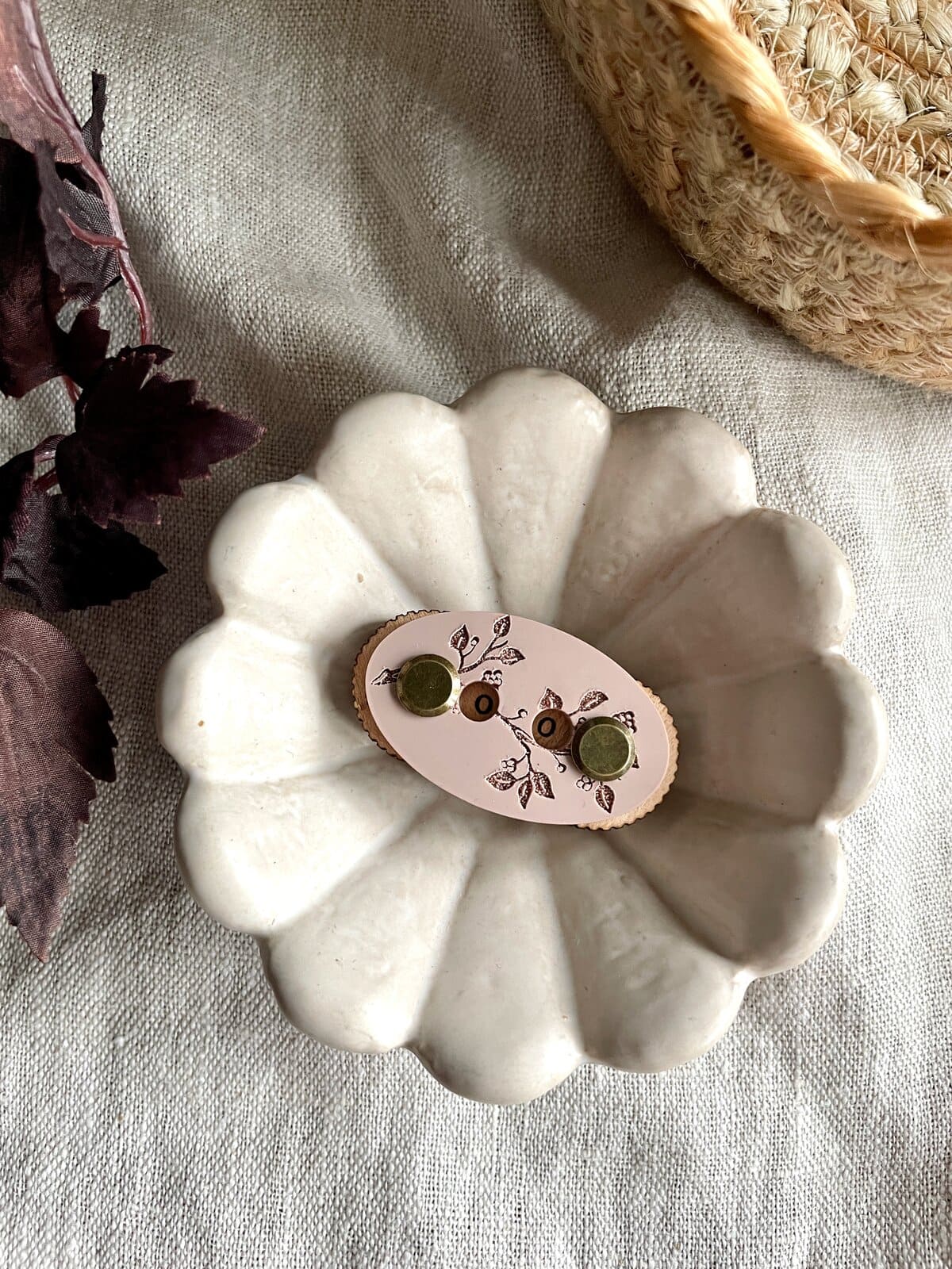 Bright white ceramic scalloped dish with decorative jewelry on natural linen background.