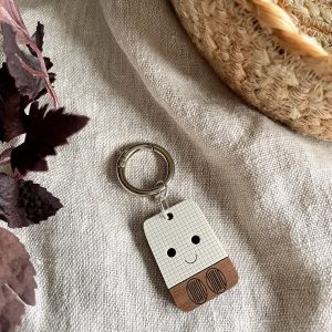 Cute robot keychain on textured fabric with woven basket and dried plant decor background.