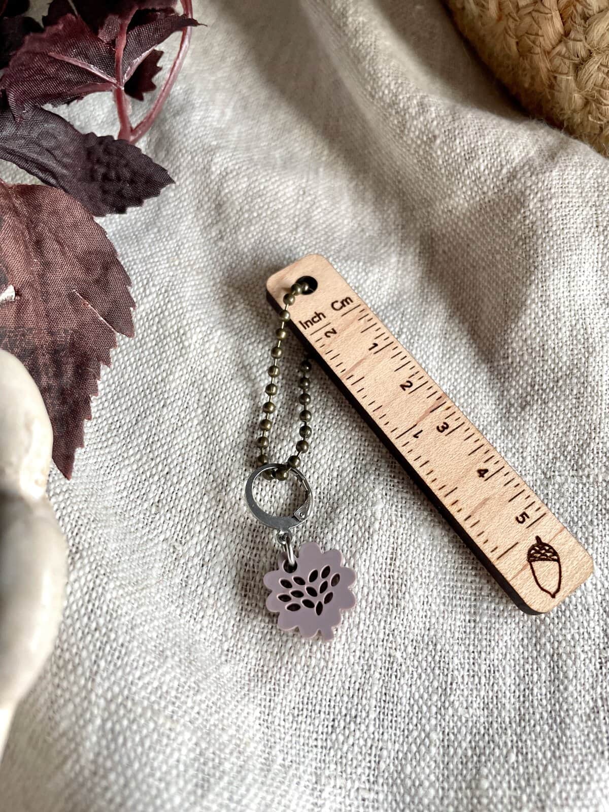 Delicate yarn-inspired jewelry charm on ball chain with ruler on fabric.