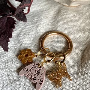 Colorful charm keychain with flower, star, and abstract designs on beige fabric background.