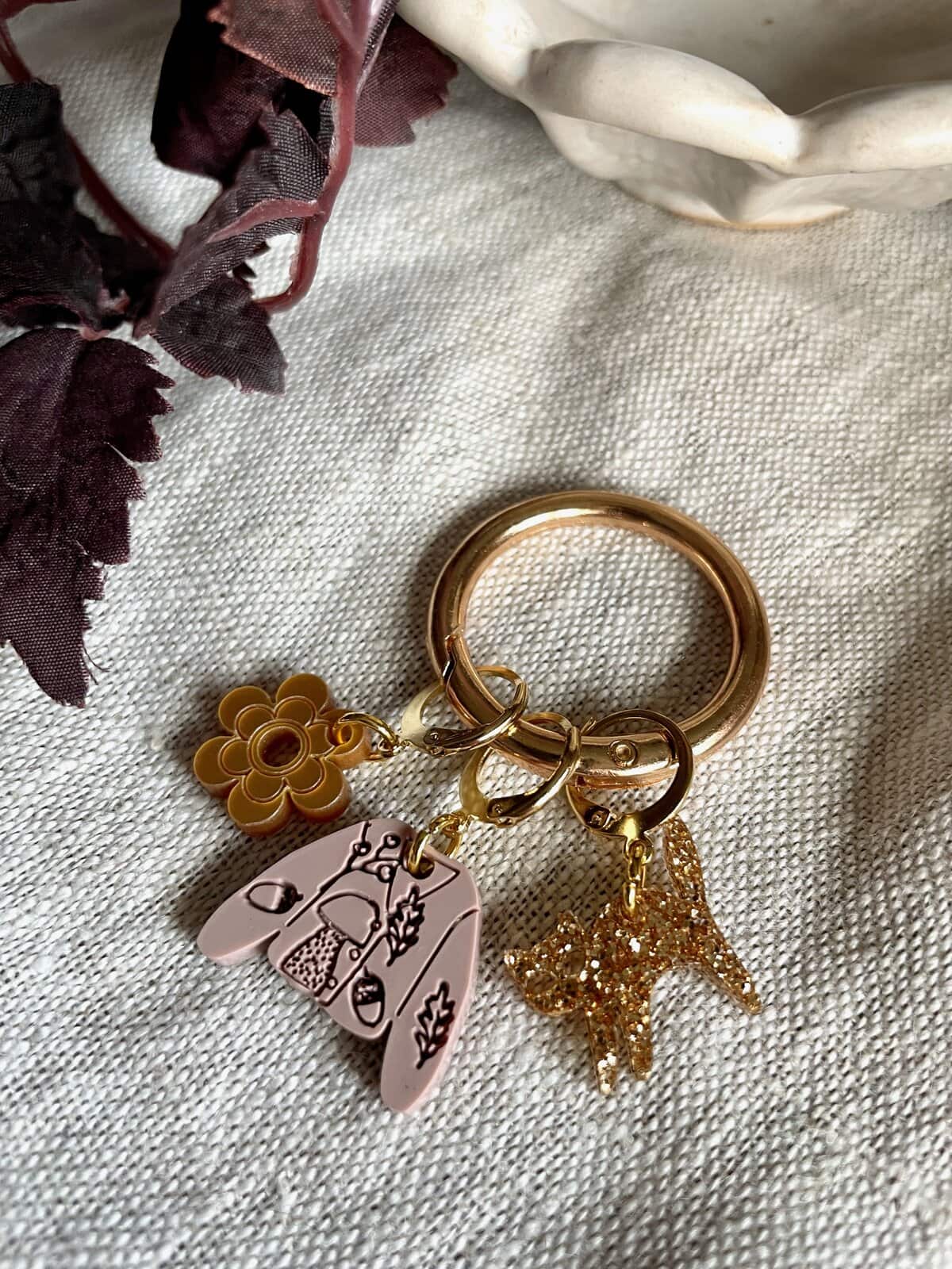 Colorful charm keychain with flower, star, and abstract designs on beige fabric background.