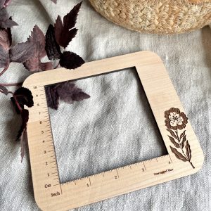 Natural wood yarn gauge with engraved flower design for knitting and crochet projects.