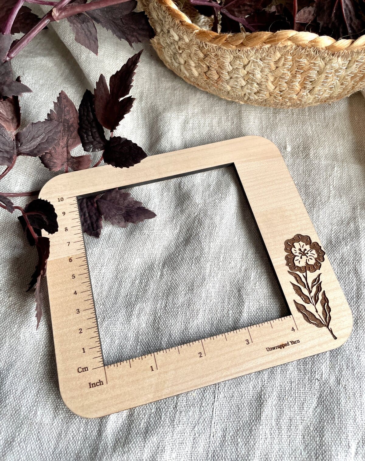 Natural wood yarn gauge with engraved flower design for knitting and crochet projects.