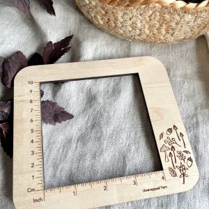 Vegan wooden yarn gauge or ruler with mushroom and plant illustrations, measuring knitting or crochet projects.