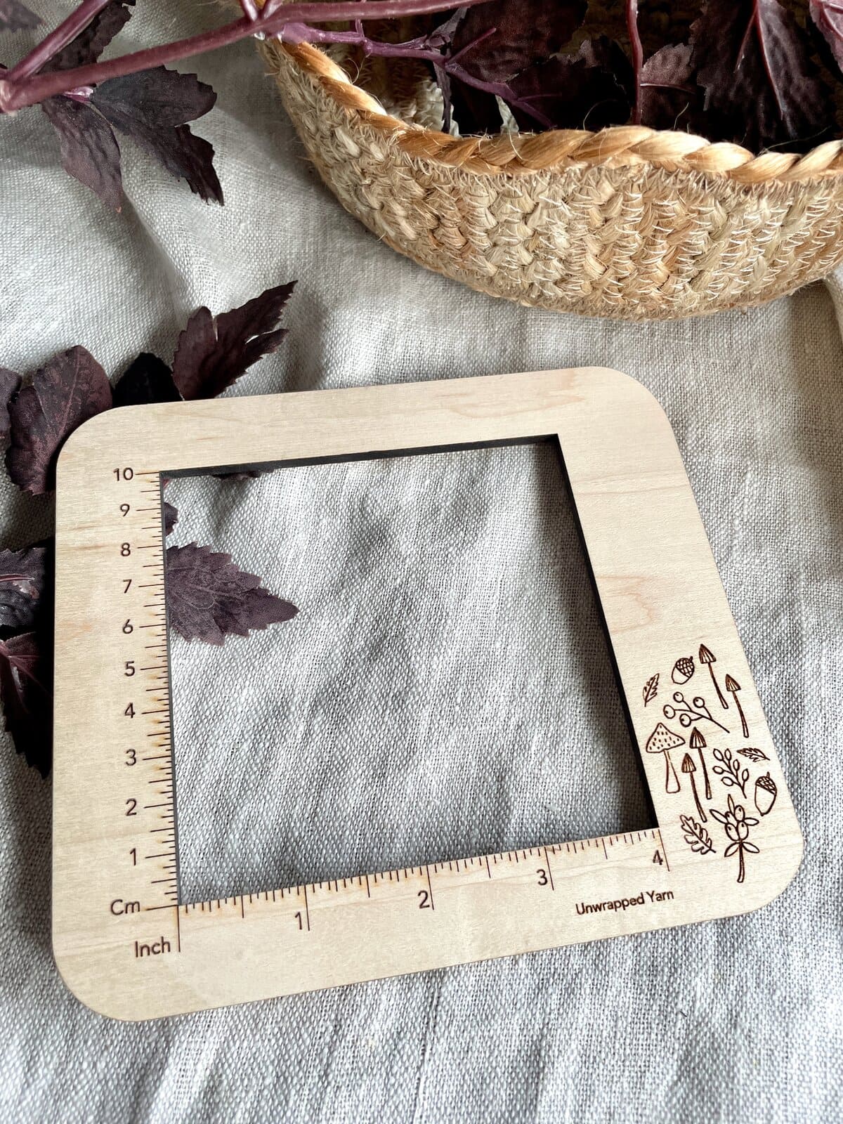 Vegan wooden yarn gauge or ruler with mushroom and plant illustrations, measuring knitting or crochet projects.