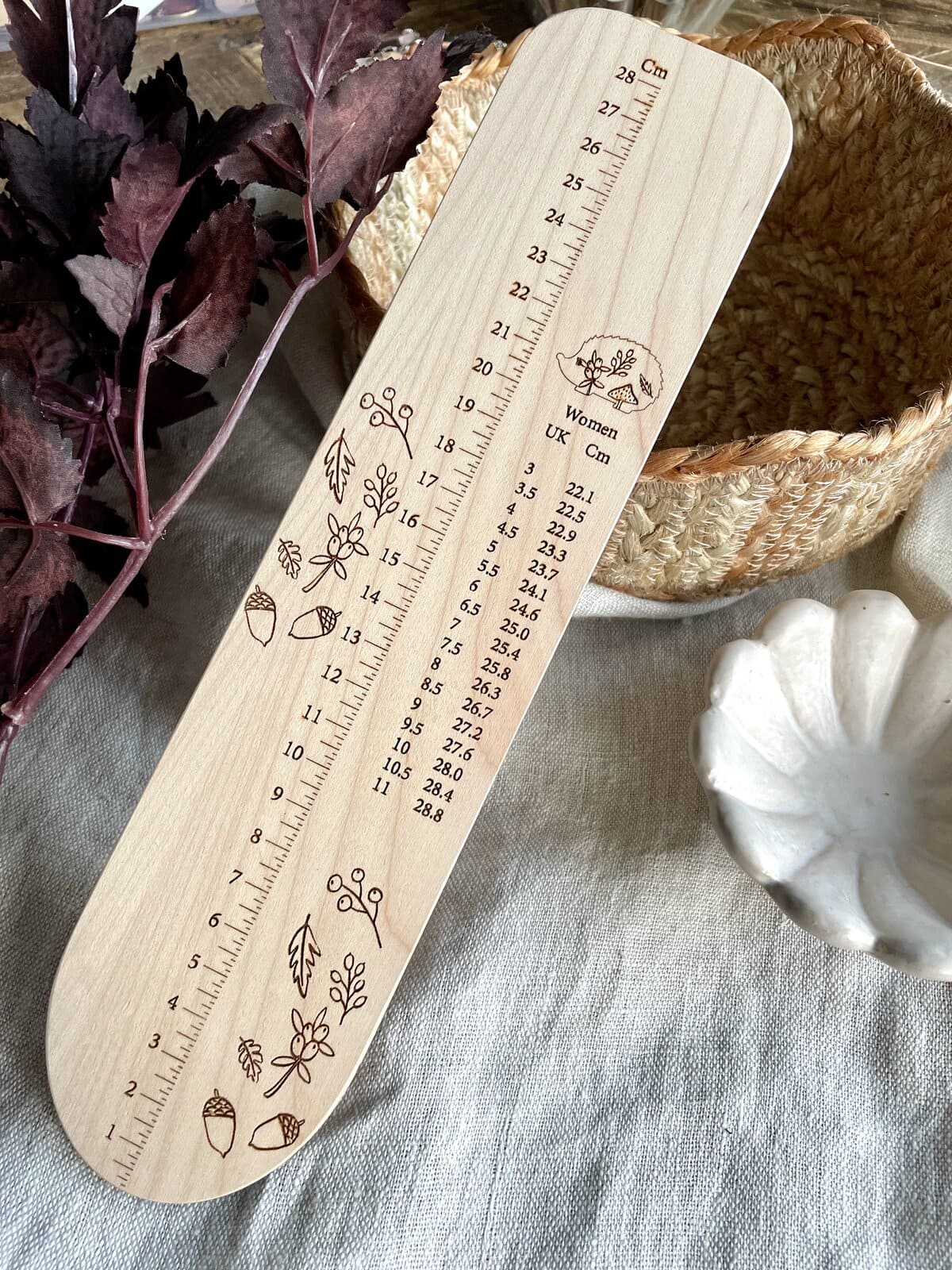 Wooden yarn measurement ruler for knitting and crochet, with decorative botanical illustrations.