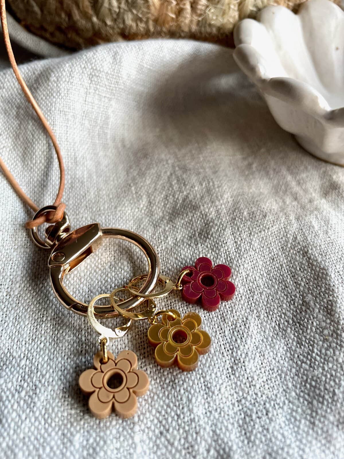 Colorful floral keychain charms with gold and pastel accents on beige fabric surface.