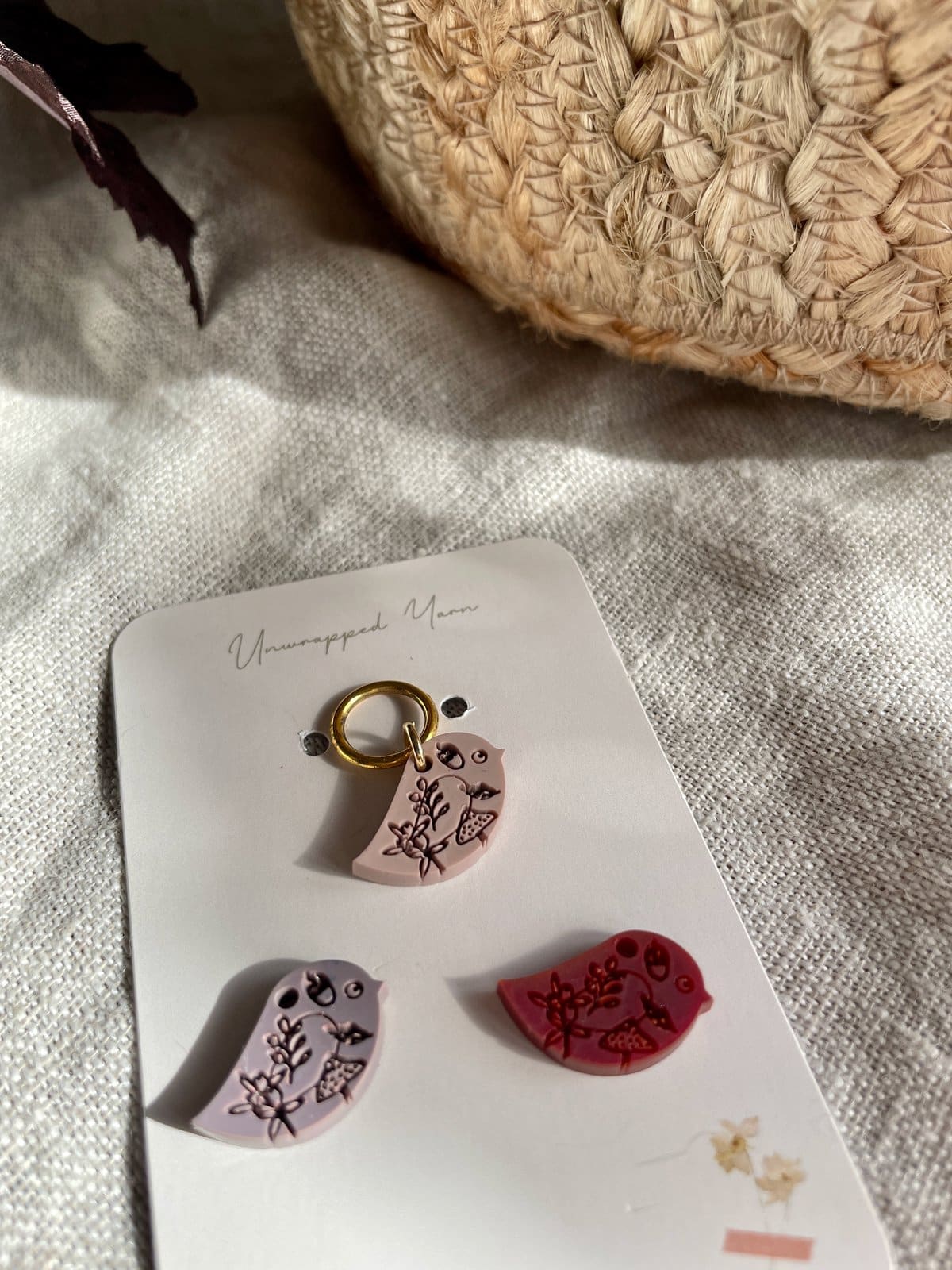 Colorful clay bird charms with floral designs on a jewelry display card, perfect for handmade accessories or craft projects.