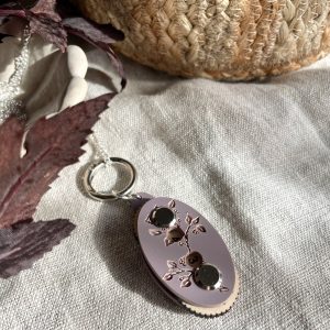 Soft pink yarn keychain with floral design and numbered buttons for knitting or crochet projects.