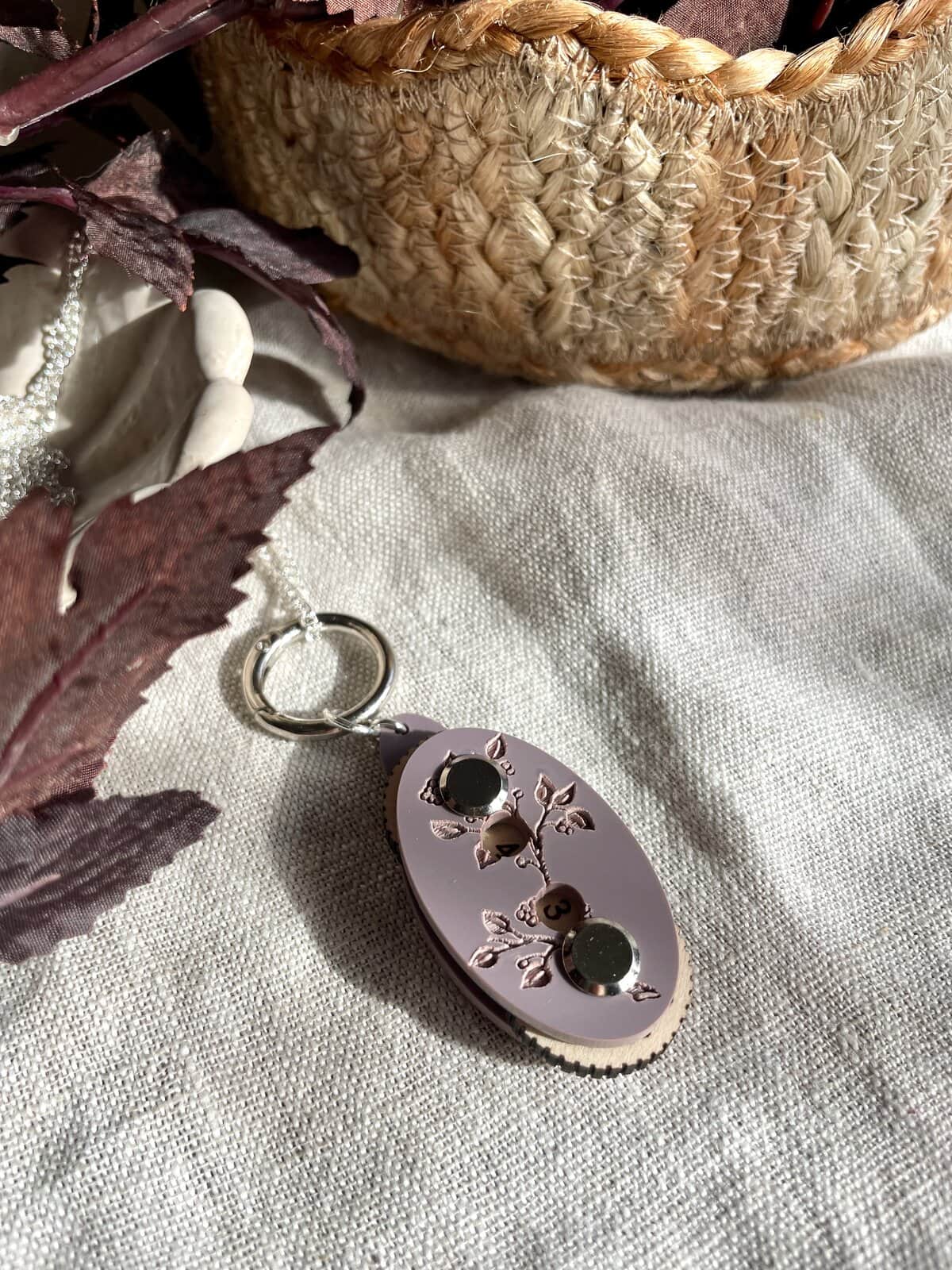 Soft pink yarn keychain with floral design and numbered buttons for knitting or crochet projects.